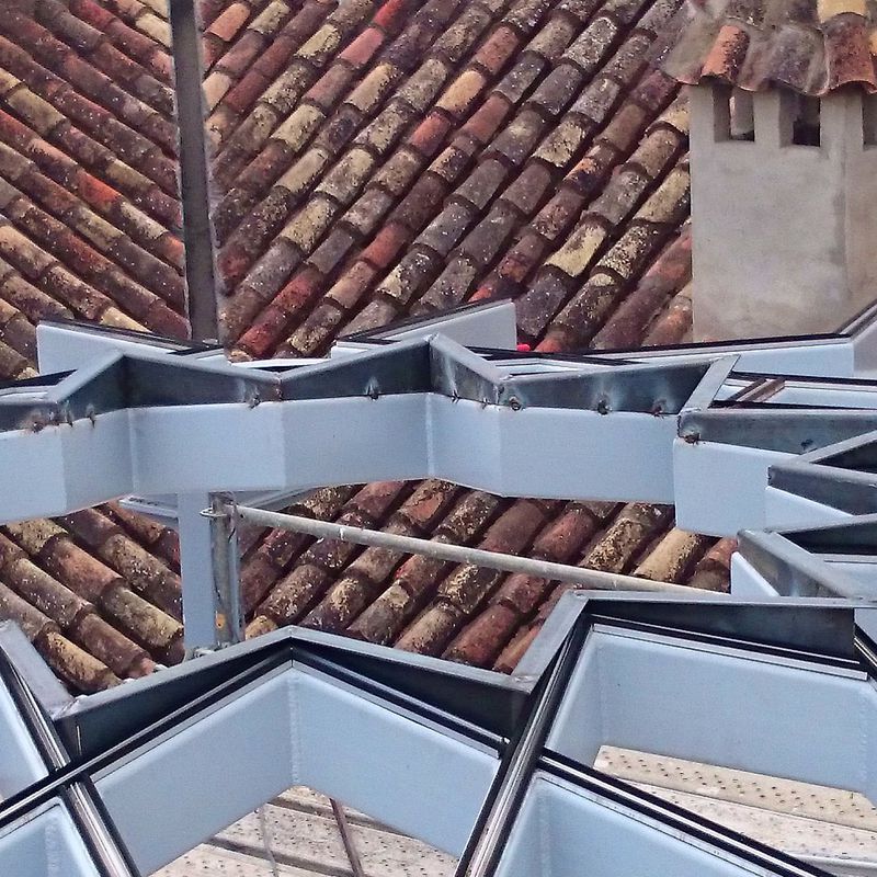 Estructura de techo de acero negro con forma de estrella formando una base totalmente plana para alojar vidrio de la misma forma adaptado a patio andaluz de palacete