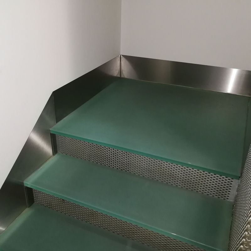 Zócalos de acero inoxidable diseñados y montados a medida para escalera de vidrio de hotel.