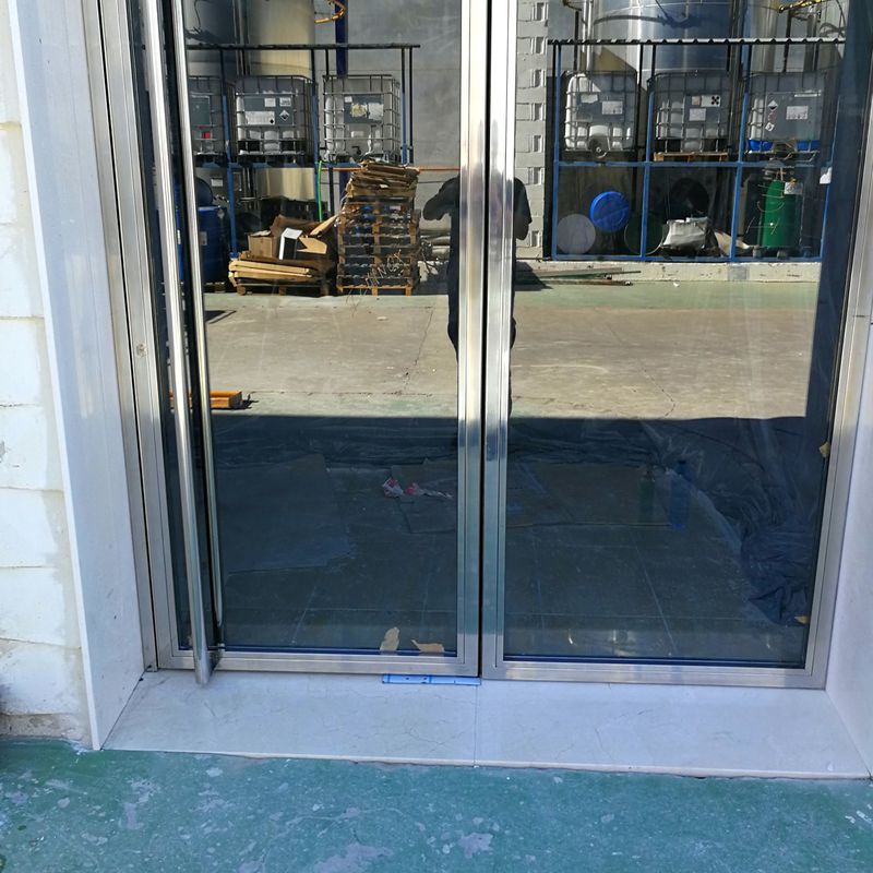 Puerta de acero inoxidable y vidrio diseñada y fabricada a medida para edificio empresarial de zona industrial.