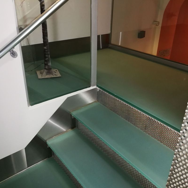 Zócalos de acero inoxidable diseñados y montados a medida para escalera de vidrio de hotel.